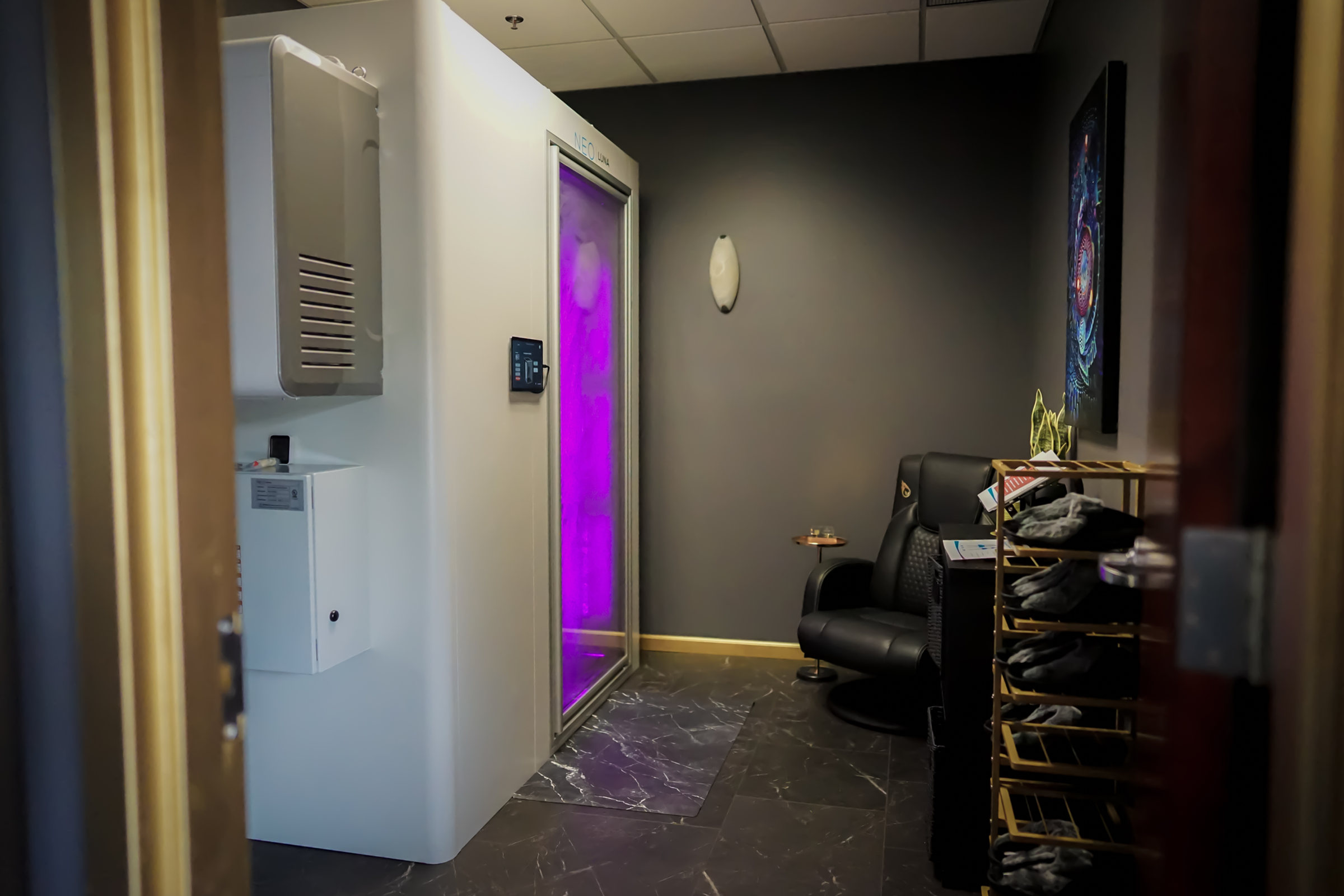 White whole body cryotherapy chamber with a purple-lit door in a charcoal treatment room