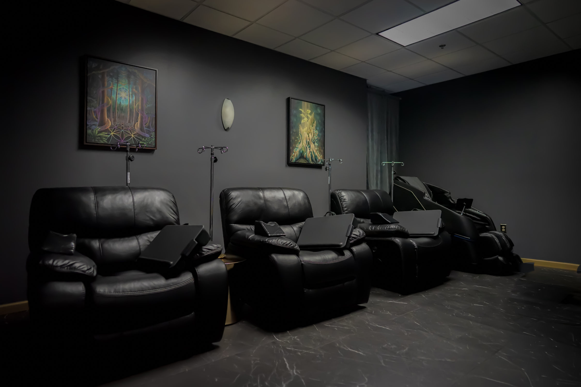IV lounge with black leather recliners, IV poles and framed art on charcoal walls